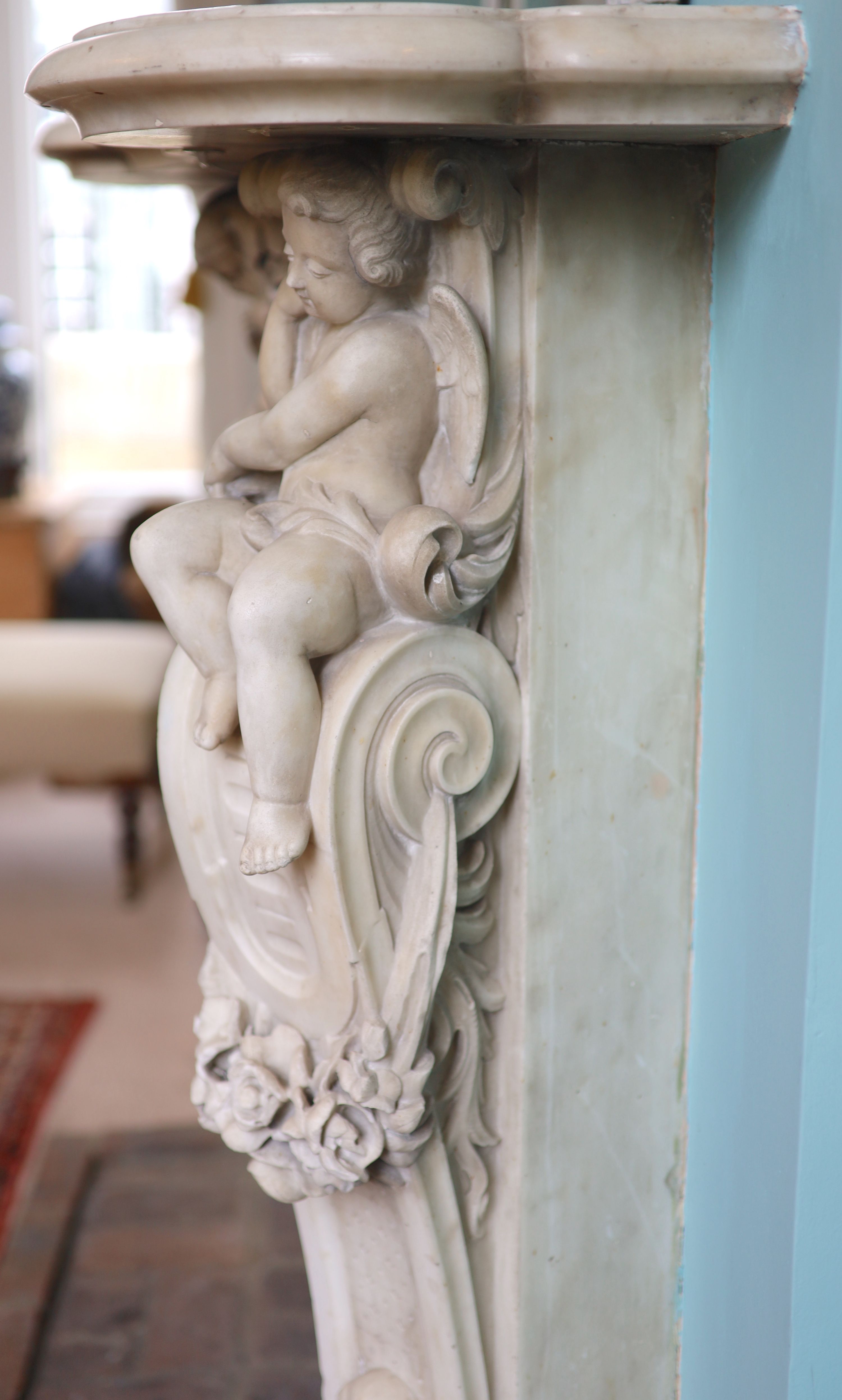 An important mid 19th century Italian white Carrara marble chimney piece, carved in the rococo taste, with seated putti, foliage swags